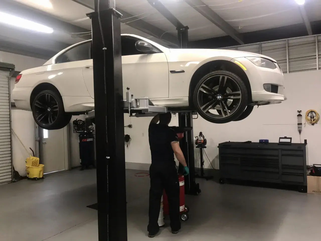 White BMW coupe raised on a lift inside Hyperformance Garage with a technician at work